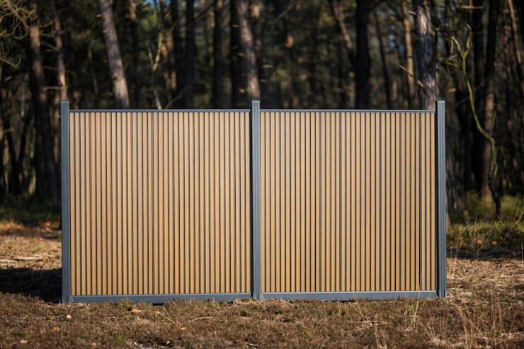 Verticale rhombus composiet schutting in teak kleur, geplaatst in een bosomgeving, model Highlander van MT Hekwerken.