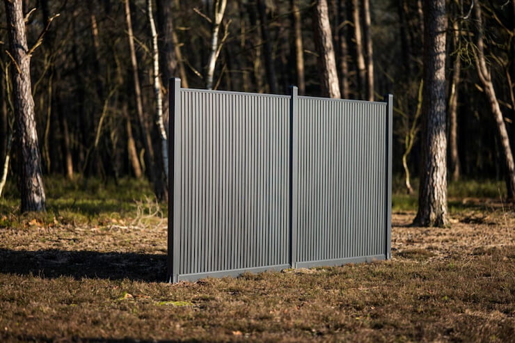 Twee panelen van een verticale zwarte rhombus composiet schutting geplaatst in een bos, model Highlander van MT Hekwerken.